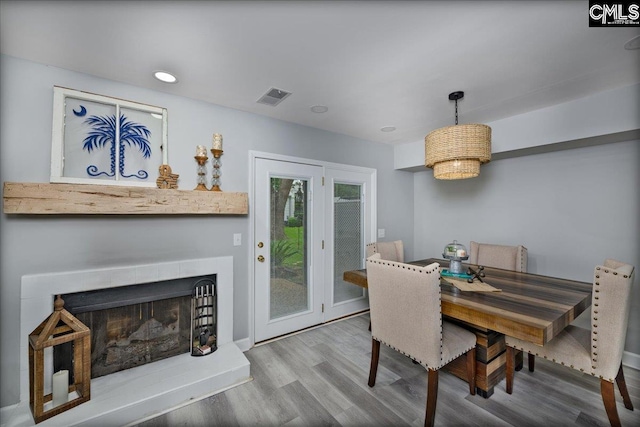 dining space with wood finished floors, a fireplace with raised hearth, and recessed lighting
