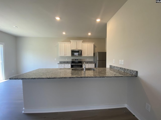 1013 Peaceful Fawn Dr, Elgin, SC 29045 - kitchen with stainless steel appliances, a sink, dark wood-style flooring, dark stone countertops, and white cabinetry