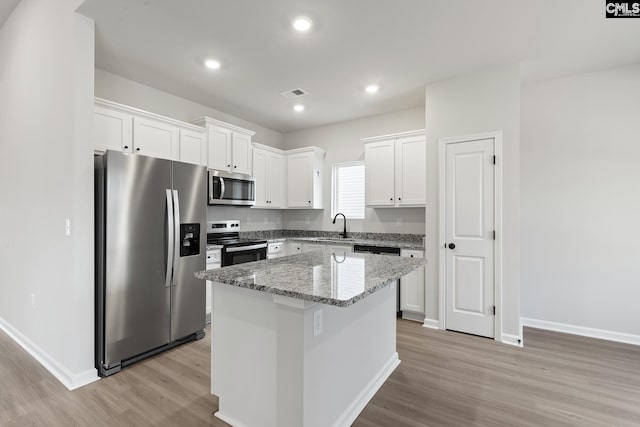 kitchen featuring appliances with stainless steel finishes, light wood-style flooring, white cabinetry, a kitchen island, and baseboards