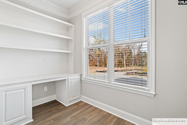 unfurnished office featuring dark wood-style flooring, built in study area, ornamental molding, baseboards, and healthy amount of natural light