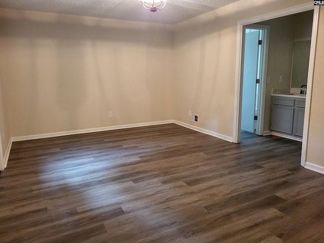 empty room with baseboards, dark wood finished floors, a textured ceiling, and a sink
