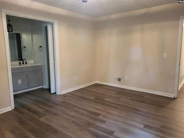 unfurnished bedroom featuring dark wood-style floors, a textured ceiling, a sink, baseboards, and ensuite bathroom