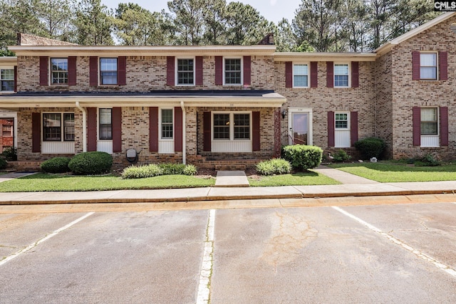 townhome / multi-family property with covered porch, brick siding, and uncovered parking