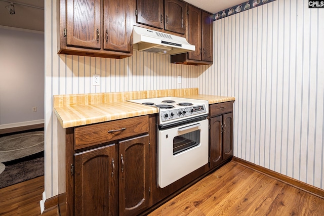 kitchen with under cabinet range hood, electric range, baseboards, light wood-style floors, and wallpapered walls