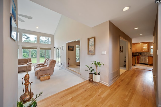 hall featuring light wood-type flooring, recessed lighting, high vaulted ceiling, and baseboards
