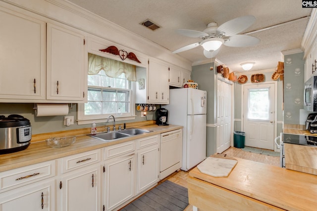 kitchen with white appliances, a sink, crown molding, healthy amount of natural light, and white cabinetry