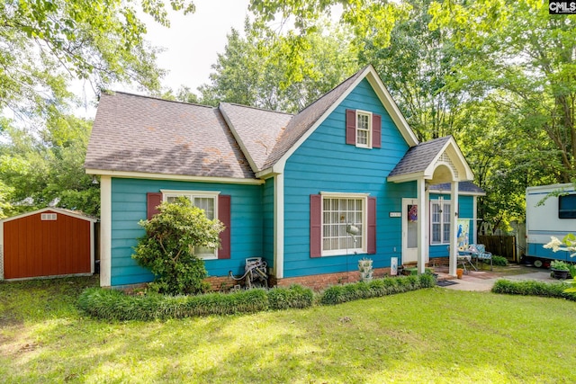 view of front of home featuring a storage shed, a shingled roof, an outdoor structure, and a front yard