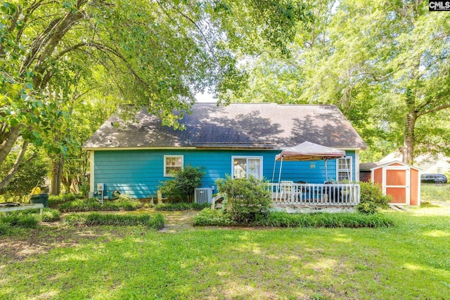 view of front of home featuring a storage unit, an outbuilding, a front yard, a deck, and a shingled roof