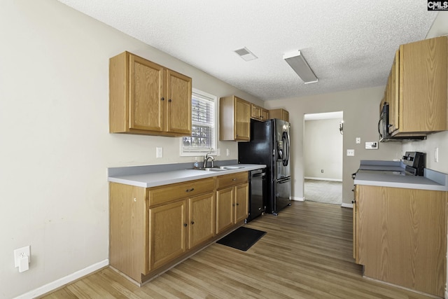 kitchen with black appliances, a sink, light wood-style flooring, light countertops, and a textured ceiling