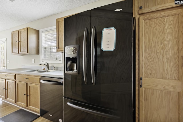kitchen featuring black refrigerator with ice dispenser, dishwasher, a sink, light countertops, and light wood finished floors