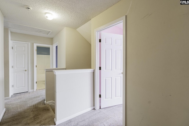 hallway with carpet flooring, a textured ceiling, an upstairs landing, and baseboards