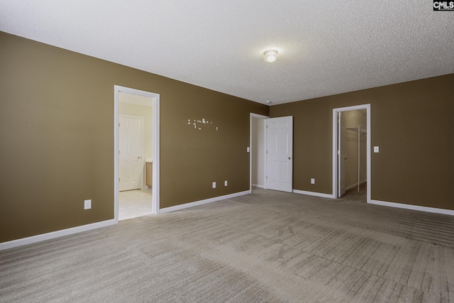 unfurnished bedroom with light colored carpet, a textured ceiling, baseboards, a spacious closet, and ensuite bath