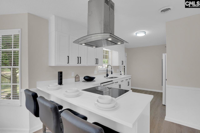 3102 Travis Ct, Columbia, SC 29204 - kitchen featuring island range hood, a sink, light wood-style flooring, white cabinets, and a breakfast bar