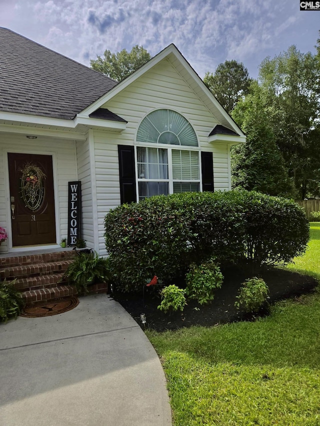property entrance with a shingled roof and a lawn