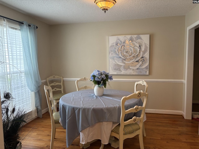 dining room with wood finished floors, healthy amount of natural light, a textured ceiling, and baseboards