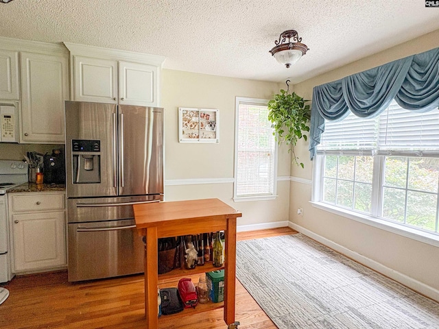 kitchen with stainless steel refrigerator with ice dispenser, plenty of natural light, a textured ceiling, light wood-type flooring, and stove