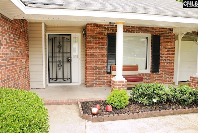 view of exterior entry featuring brick siding, a porch, and a shingled roof