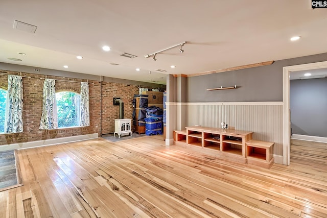109 Broad Bluff Pt, Irmo, SC 29063 - exercise room featuring a wood stove, brick wall, hardwood / wood-style flooring, a wainscoted wall, and rail lighting