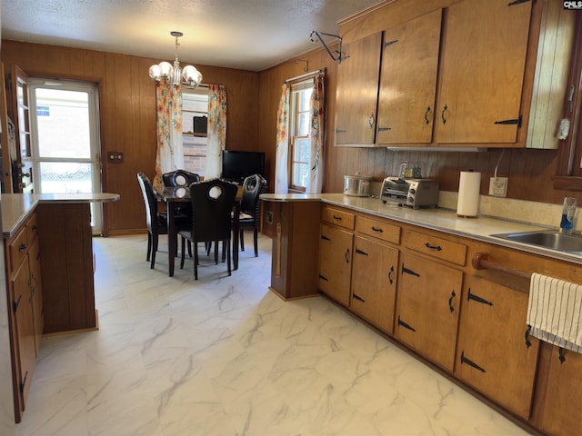 2313 Omega Dr, Columbia, SC 29223 - kitchen featuring brown cabinets, a chandelier, a textured ceiling, light countertops, and wooden walls