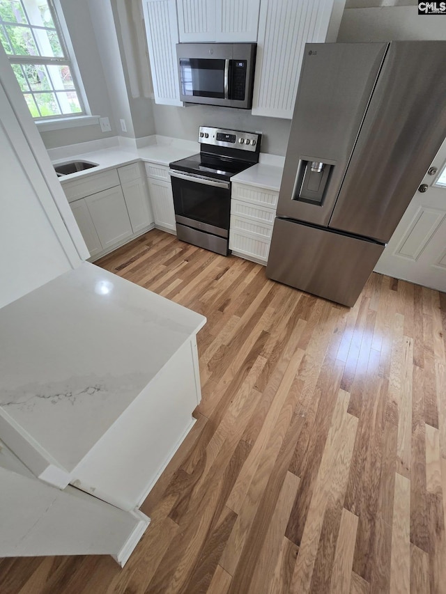 kitchen featuring appliances with stainless steel finishes, light wood-style flooring, light countertops, white cabinets, and a sink
