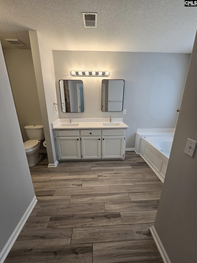 full bathroom featuring wood finished floors, toilet, a textured ceiling, a bath, and double vanity