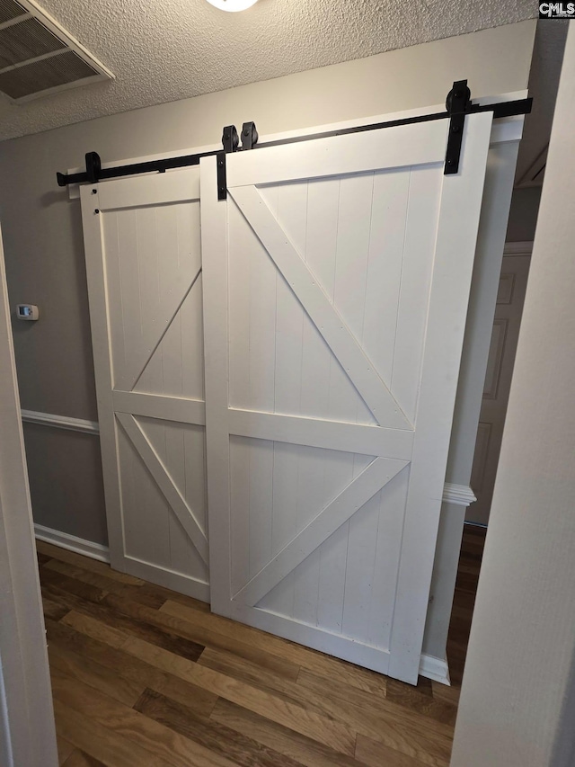 detailed view of a barn door, wood finished floors, and a textured ceiling