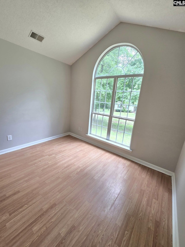 spare room with light wood finished floors, baseboards, lofted ceiling, and a textured ceiling