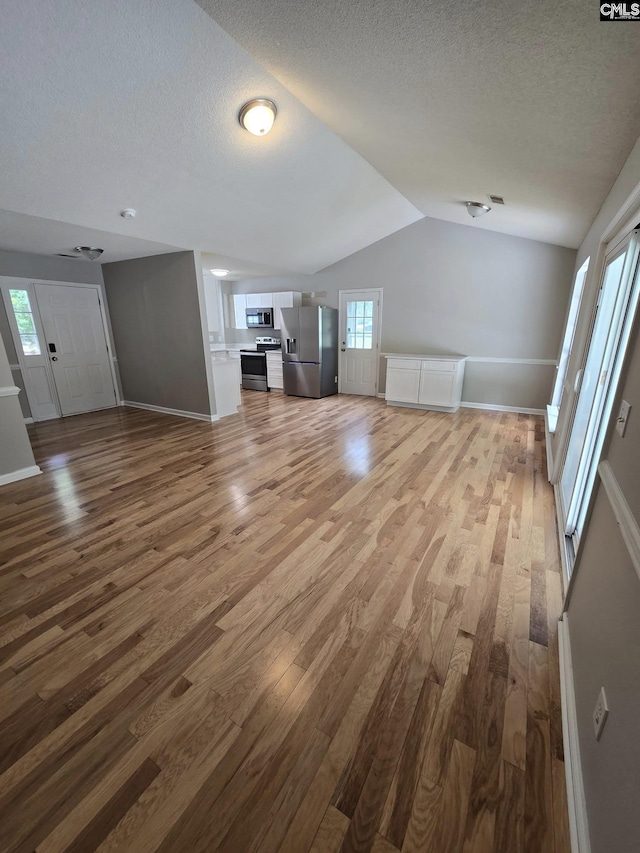 unfurnished living room featuring wood finished floors, a textured ceiling, vaulted ceiling, and baseboards