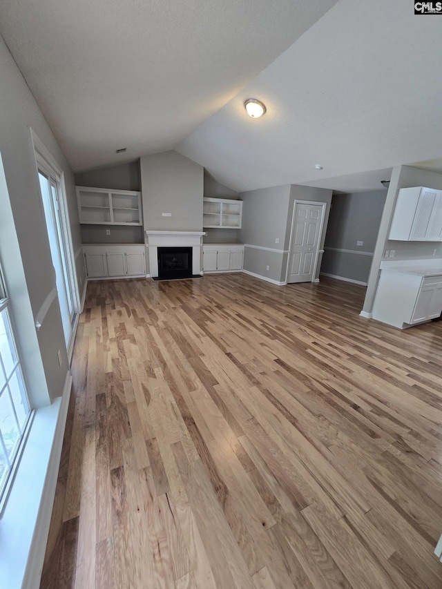 unfurnished living room with light wood-style flooring, vaulted ceiling, baseboards, and a fireplace