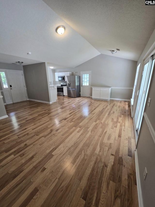 unfurnished living room featuring a textured ceiling, wood finished floors, vaulted ceiling, and baseboards