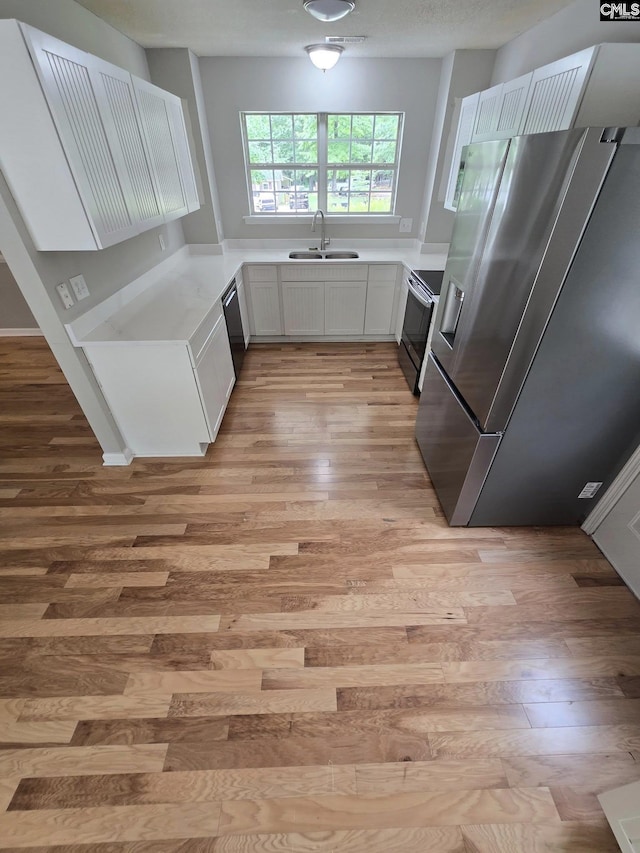 kitchen featuring stainless steel fridge, a sink, light wood finished floors, and range with electric stovetop