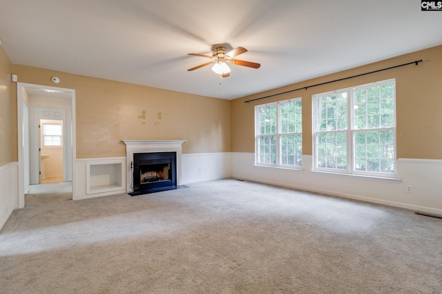 1113 Walden Place Dr, Elgin, SC 29045 - unfurnished living room featuring a ceiling fan, plenty of natural light, wainscoting, a fireplace with flush hearth, and carpet floors