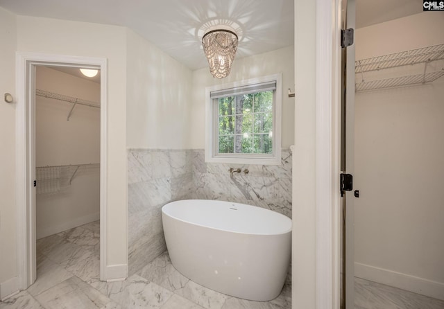 67 Ole Still Ln, Elgin, SC 29045 - bathroom featuring marble look tile flooring, a spacious closet, a freestanding tub, tile walls, and wainscoting