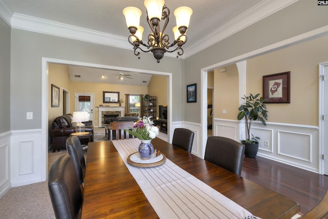 301 Spring Mist Ct, Lexington, SC 29072 - dining space featuring a fireplace, a chandelier, crown molding, wainscoting, and ceiling fan