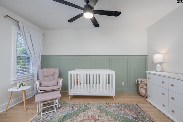 315 Bent Pine Dr, Columbia, SC 29212 - bedroom with a decorative wall, a crib, light wood-style flooring, wainscoting, and a ceiling fan