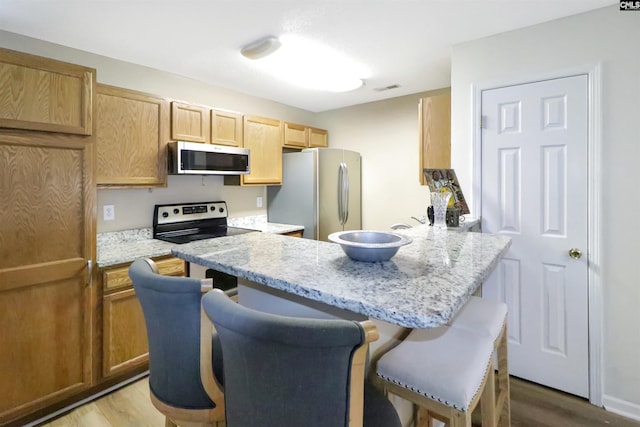 1306 Waverly Place Dr, Columbia, SC 29223 - kitchen featuring stainless steel appliances, a kitchen breakfast bar, wood finished floors, a peninsula, and light stone counters
