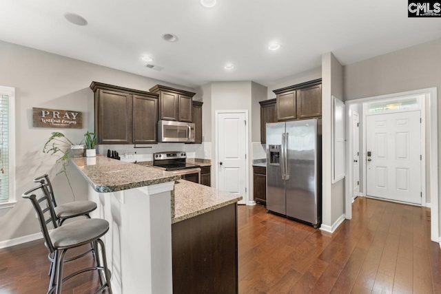 300 Brookland Way W, Columbia, SC 29169 - kitchen featuring stainless steel appliances, dark brown cabinets, a peninsula, a kitchen bar, and light stone countertops