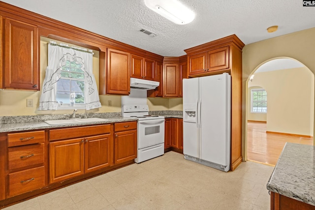 114 Quattlebaum Ave, Ridge Spring, SC 29129 - kitchen with white appliances, a sink, under cabinet range hood, brown cabinetry, and arched walkways