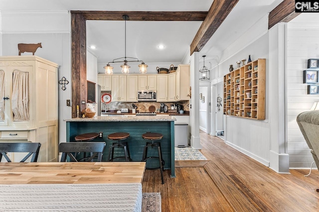 2909 Columbia Ave, Columbia, SC 29201 - kitchen featuring stainless steel microwave, cream cabinetry, light wood-style flooring, tasteful backsplash, and a peninsula