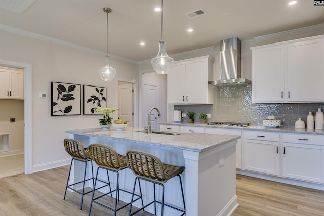 821 Oak Valley Dr, Blythewood, SC 29016 - kitchen with wall chimney range hood, stainless steel gas cooktop, light wood-type flooring, tasteful backsplash, and an island with sink