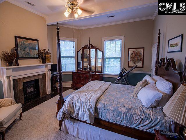 1220 Calhoun St, Newberry, SC 29108 - bedroom with a fireplace with flush hearth, crown molding, multiple windows, carpet, and a ceiling fan