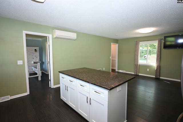 214 Mac St, Leesville, SC 29070 - kitchen with an AC wall unit, a textured ceiling, white cabinetry, dark wood-style floors, and a kitchen island