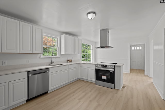 4405 Palmetto Ave, Columbia, SC 29203 - kitchen featuring appliances with stainless steel finishes, wall chimney range hood, light wood-type flooring, light countertops, and white cabinetry