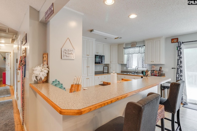 1037 Ridgeview Cir, Elgin, SC 29045 - kitchen with black microwave, a textured ceiling, a kitchen bar, a peninsula, and light wood-style floors