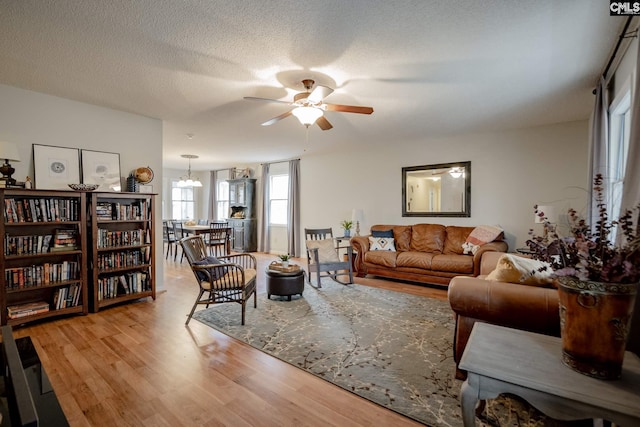 living room featuring light hardwood / wood-style floors, a textured ceiling, and ceiling fan with notable chandelier