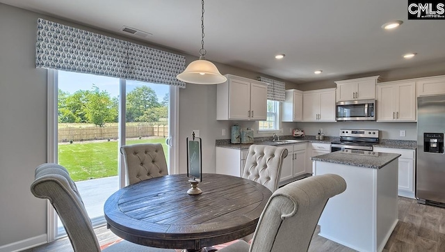 kitchen with a kitchen island, decorative light fixtures, hardwood / wood-style floors, appliances with stainless steel finishes, and white cabinetry