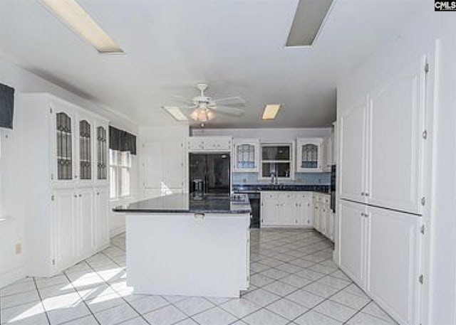 kitchen featuring a center island, black refrigerator, ceiling fan, light tile floors, and white cabinetry