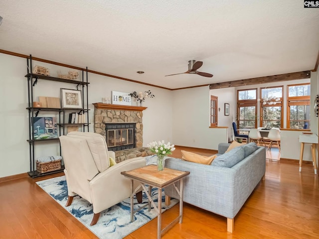 living room with a textured ceiling, a stone fireplace, ceiling fan, and light hardwood / wood-style flooring