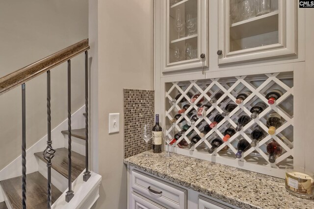 bar featuring white cabinets, backsplash, and light stone countertops