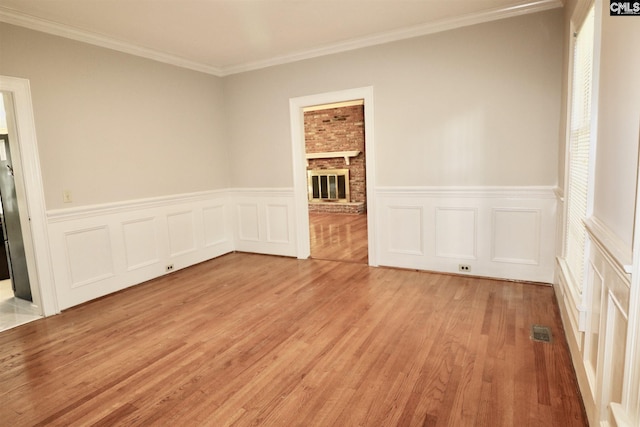 unfurnished room with light hardwood / wood-style flooring, crown molding, brick wall, and a brick fireplace